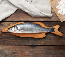 fresh whole sea bass fish on brown cutting board