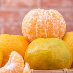 Peeled tangerines in a bamboo sieve basket on dark wooden table with red brick wall background, Chinese lunar new year fruit design concept, close up.