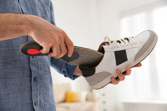 Man putting orthopedic insole into shoe at home, closeup
