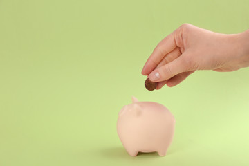Woman putting coin into piggy bank on green background, closeup