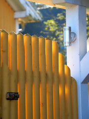 a yellow fence out of wood separates the garden from the street. A silver lamp clears it up.