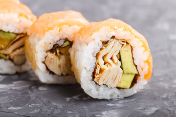 Japanese maki sushi rolls with salmon, avocado and omelette on black concrete background. Side view.