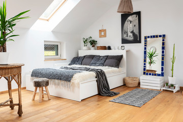 Modern bedroom interior of living room in the attic with double bed and grey  pillows and bedspread. Wooden floor and furniture in bright cozy indoors.
