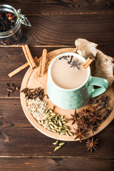 Clay cup on a wooden board on a dark background. A cup of masala tea. Spices cloves, fennel, cinnamon, cardamom, milk.