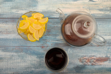 Marmalade lemon slices, a glass of black tea and a teapot with brewed tea on a wooden background. Sweet dessert. Close up.