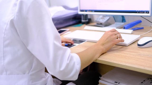 Woman doctor surgeon in white uniform types on the computer keyboard the diagnosis and examination results. Hands close up. Modern medical technologies. Healthcare and medicine. 4k footage.