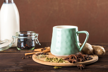 Obraz na płótnie Canvas Clay cup on a wooden board on a dark background. A cup of masala tea. Spices cloves, fennel, cinnamon, cardamom, milk.