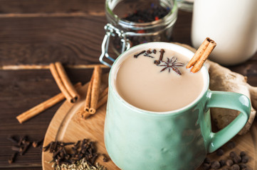 Clay cup on a wooden board on a dark background. A cup of masala tea. Spices cloves, fennel,...