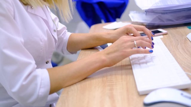 Woman doctor surgeon in white uniform types on the computer keyboard the diagnosis and examination results. Hands close up. Modern medical technologies. Healthcare and medicine. 4k footage.