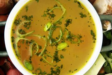 Broth with carrots, onions various fresh vegetables in a pot - colorful fresh clear spring soup. Rural kitchen scenery vegetarian bouillon stock