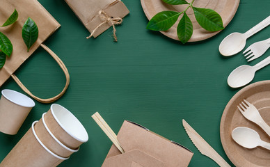 Recycled Eco-friendly disposable tableware made of paper on a green background. Wooden spoons,...