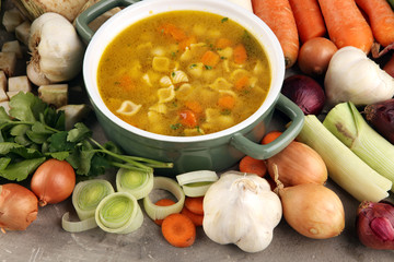 Broth with noodles and carrots, various fresh vegetables in a pot - colorful fresh clear spring soup. Rural kitchen scenery vegetarian bouillon stock