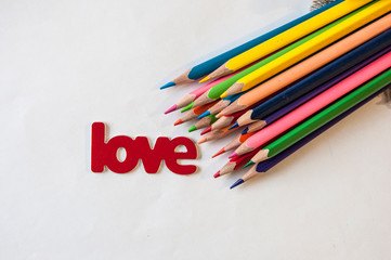 Word LOVE with decorative red heart and  colorful  pencils, flat lay