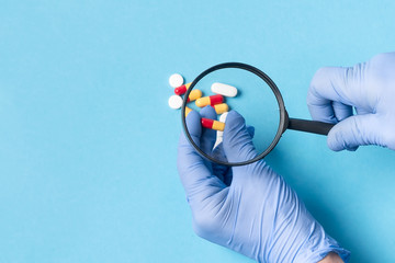 Concept - pharmaceutical testing, testing of medicines, magnifying glass, tablets on a blue...