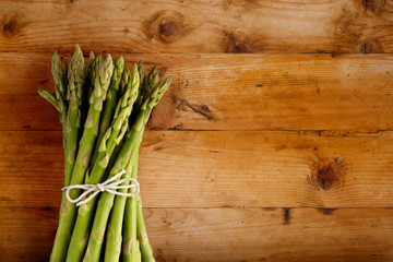 A fresh bunch of asparagus, tied with a string bow, shot on a wooden background, with copy space