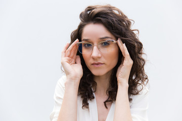 Portrait of serious positive female professional in glasses. Wavy haired young woman in casual shirt standing isolated over white background. Female portrait concept