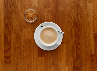 A cappuccino coffee, shot on a panelled wooden worktop, with brown sugar in a bowl, with copy space.