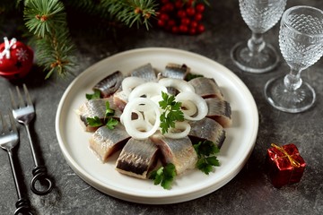 Slices of herring with onions, butter and vinegar on a white dish.