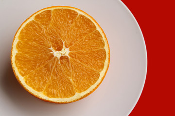 juicy yellow orange lies on a white plate on a red table, top view, copy space