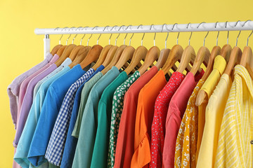 Bright clothes hanging on rack against yellow background. Rainbow colors