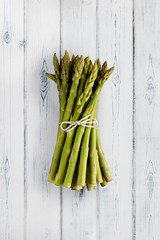 A portrait view of fresh bunch of asparagus, tied with a string bow, shot on a distressed white wooden background, with copy space