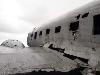 remains of a wing and part of the rusty cabin of an old abandoned military plane on the coast of Iceland. in the background you can see a cloudy sky with gray gradients.