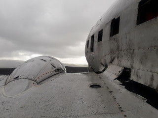 remains of a wing and part of the rusty cabin of an old abandoned military plane on the coast of Iceland. in the background you can see a cloudy sky with gray gradients.