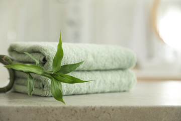Stack of clean towels and bamboo sprout on table in bathroom