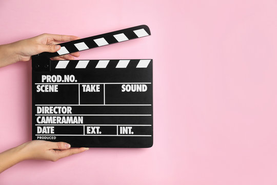 Woman holding clapperboard on pink background, closeup with space for text. Cinema production