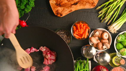 Roasting fresh meat in a wok, on a background with vegetables