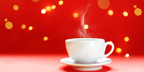 Steaming coffee cup over red background. Festive atmosphere with warm bokeh lights