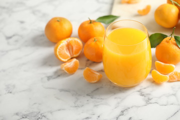 Glass of fresh tangerine juice and fruits on marble table. Space for text