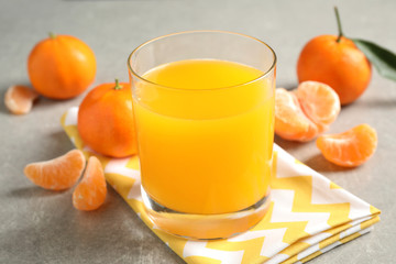 Glass of fresh tangerine juice and fruits on light grey table