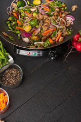 Roasting meat with vegetables, on a black wooden background. Cooking, gastronomy. Vertical frame. Delicious and healthy food, with space for an inscription.