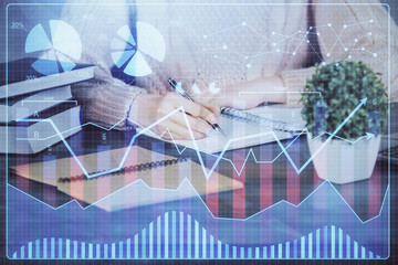 Forex graph on hand taking notes background. Concept of research. Double exposure