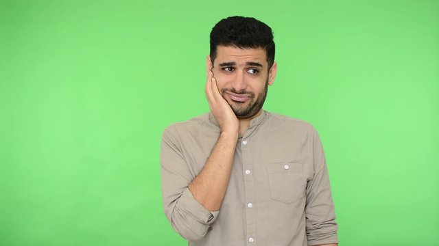 Unhappy pensive brunette man in shirt scratching his unshaven chin, thinking over idea, pondering difficult question, having doubts, hesitation. indoor studio shot, green background, chroma key
