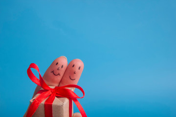 Funny fingers couple holding present gift box against blue background. Happy family celebrating concept for Christmas or New Years day with copy space for ad text