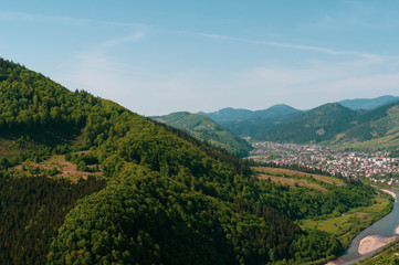 Fototapeta na wymiar top view of landscape of valley with river, town and sky among high mountains covered with green trees