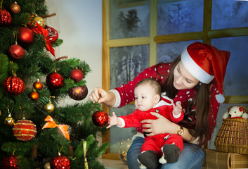Young beautiful girl with a small child near a Christmas tree on a background of a snowy window