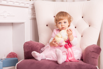Cute little girl in an elegant dress sits in an armchair