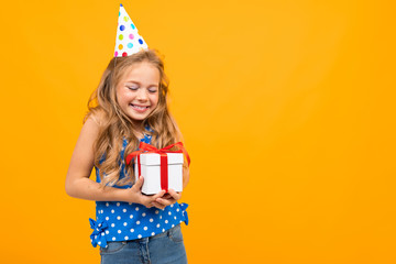 smiling girl in a holiday hat holds a gift box on an orange studio background with copy space