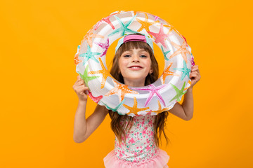 little girl in a swimsuit with a swimming circle on an orange background