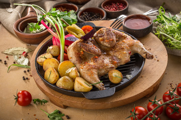 Chicken tobacco on metal pan with grilled potato and tomato sauce on wooden table