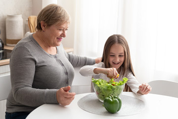 Grandmother and teen granddaughter prepare healthy food in the kitchen. Smiley family preparing a salad together