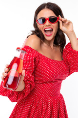 stylish brunette girl in sunglasses with a glass of cocktail is dancing on a white background