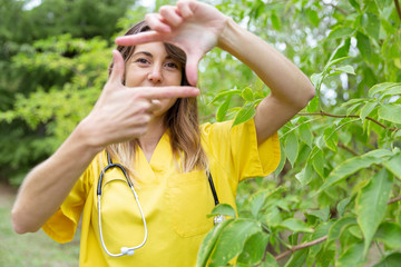 Mujer enfermera joven con uniforme amarillo y estetoscopio colgado del cuello enmarca su cara con...
