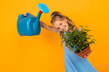 smiling girl in a dress holds a plant and a watering can on an orange background