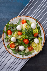 Fresh salad with tomato, arugula, lettuce and mozzarella on a plate. Concept of healthy and diet food. Top view.