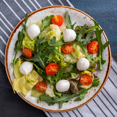 Fresh salad with tomato, arugula, lettuce and mozzarella on a plate. Top view. Closeup