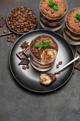 Classic tiramisu dessert in a glass cup and pieces of chocolate on dark concrete background